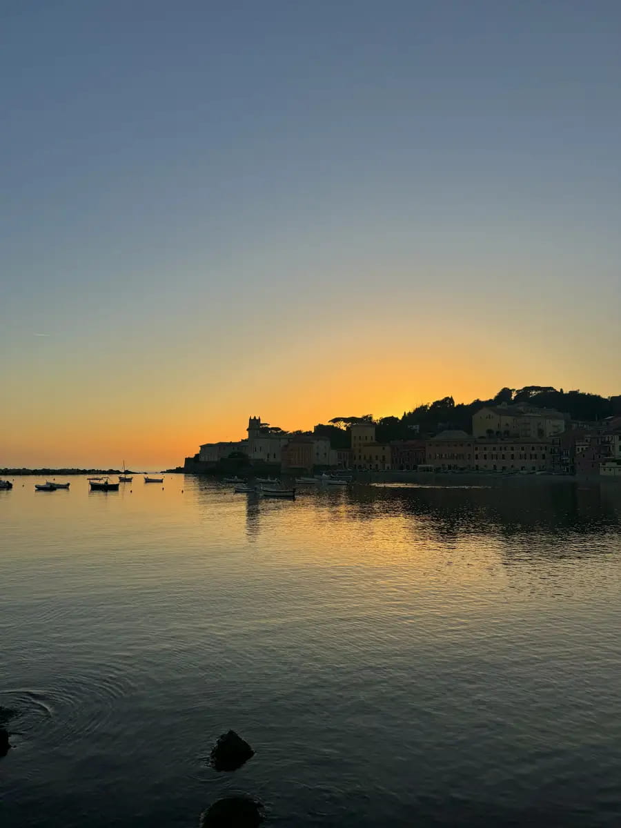 sunset in baia del silenzio with the silhouette of the colourful pastel buildings reflected on the water