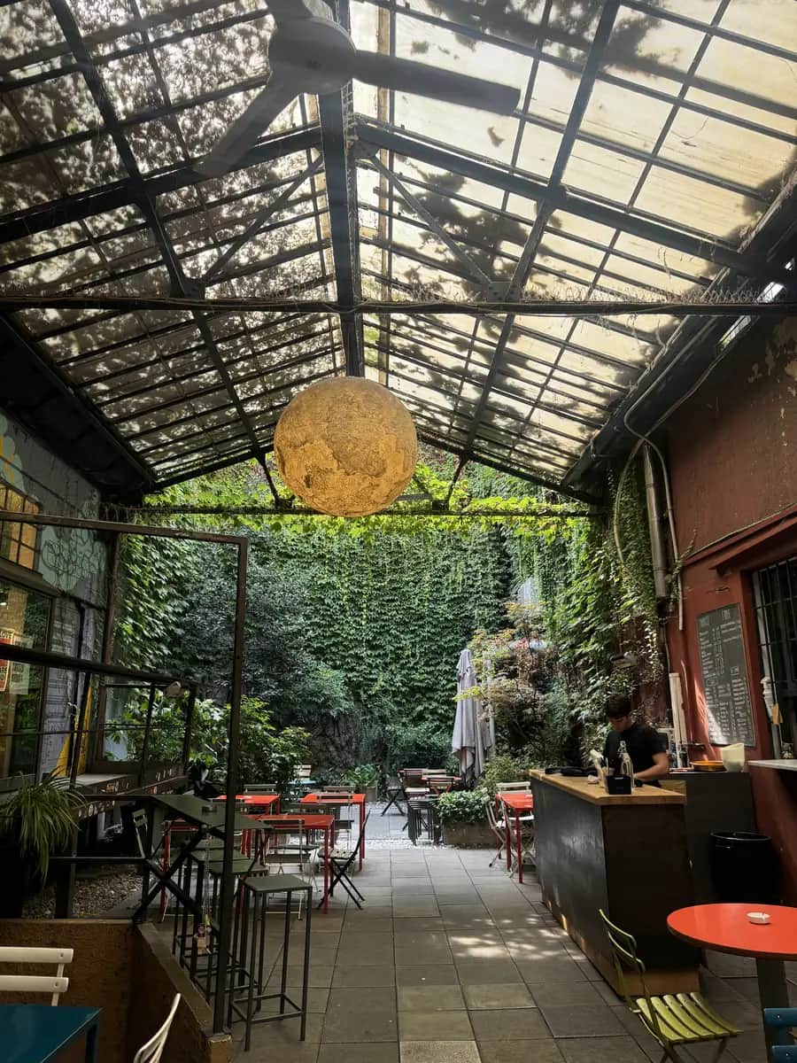 A large industrial courtyard at Bar Frida in Milan with ivy covered walls and trees growing through the outdoor seating area.