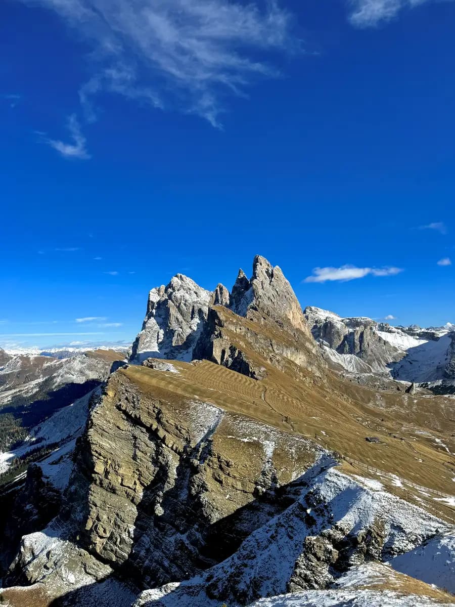 The iconic Seceda ridgeline viewpoint in the Dolomites, showing the steep, jagged diagonal cliffs dropping into the green and snowy valley below