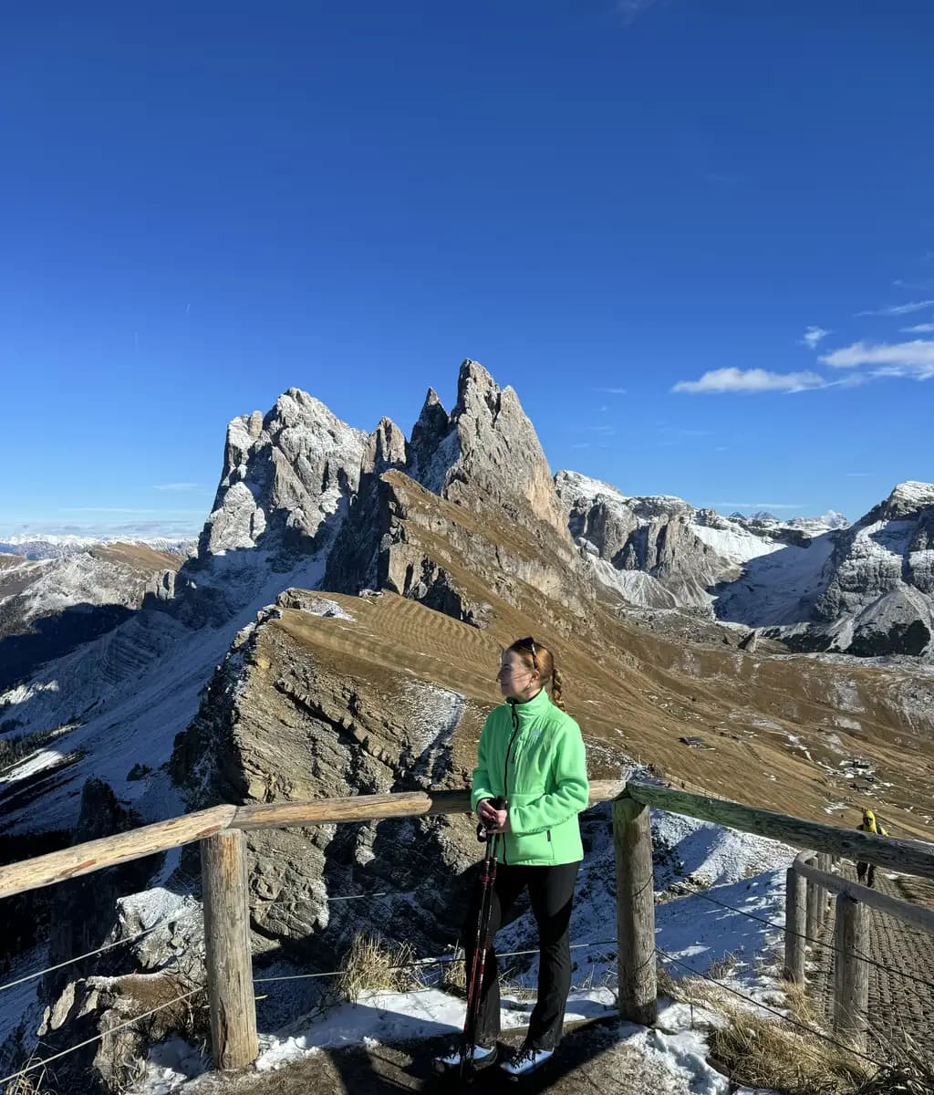 a hiker at the iconic Seceda ridgeline viewpoint in the Dolomites, showing the steep, jagged diagonal cliffs dropping into the green valley below