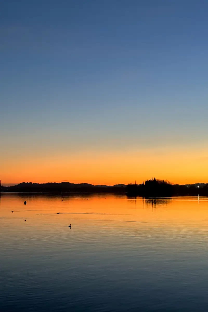 A scenic sunset over lake pusiano with the outline of the cypress island. the yellow and orange of the sky reflecting in the water of the Lake