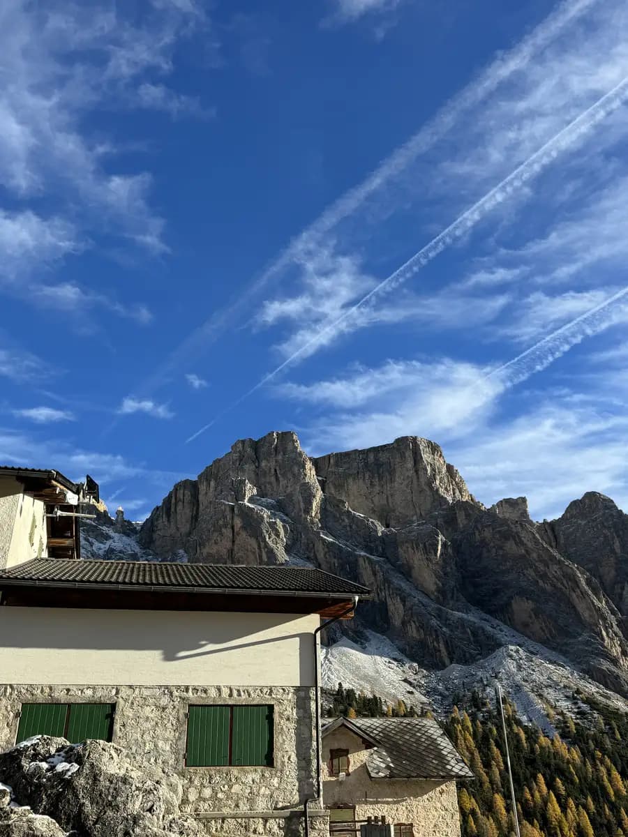 Rifugio Firenze mountain hut sitting in a green alpine meadow with the jagged peaks of the Dolomites rising dramatically behind it.