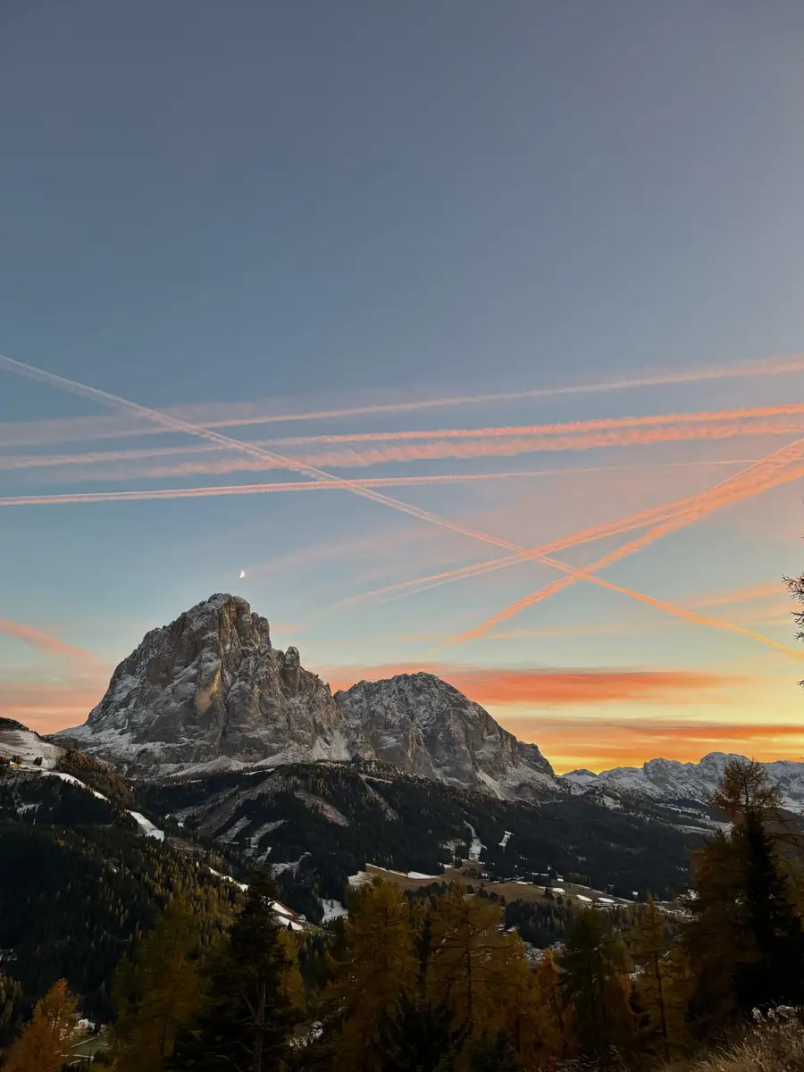The Sassolungo mountain peak at sunset, with the sky glowing in vibrant shades of pink and orange behind the jagged rock formation.