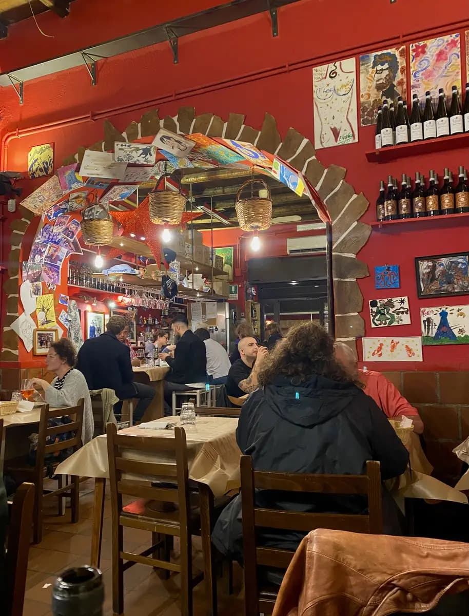 The lively interior of Trattoria Al Ferro di Cavallo in Palermo, featuring vibrant red walls covered from top to bottom in various drawings and sketches.