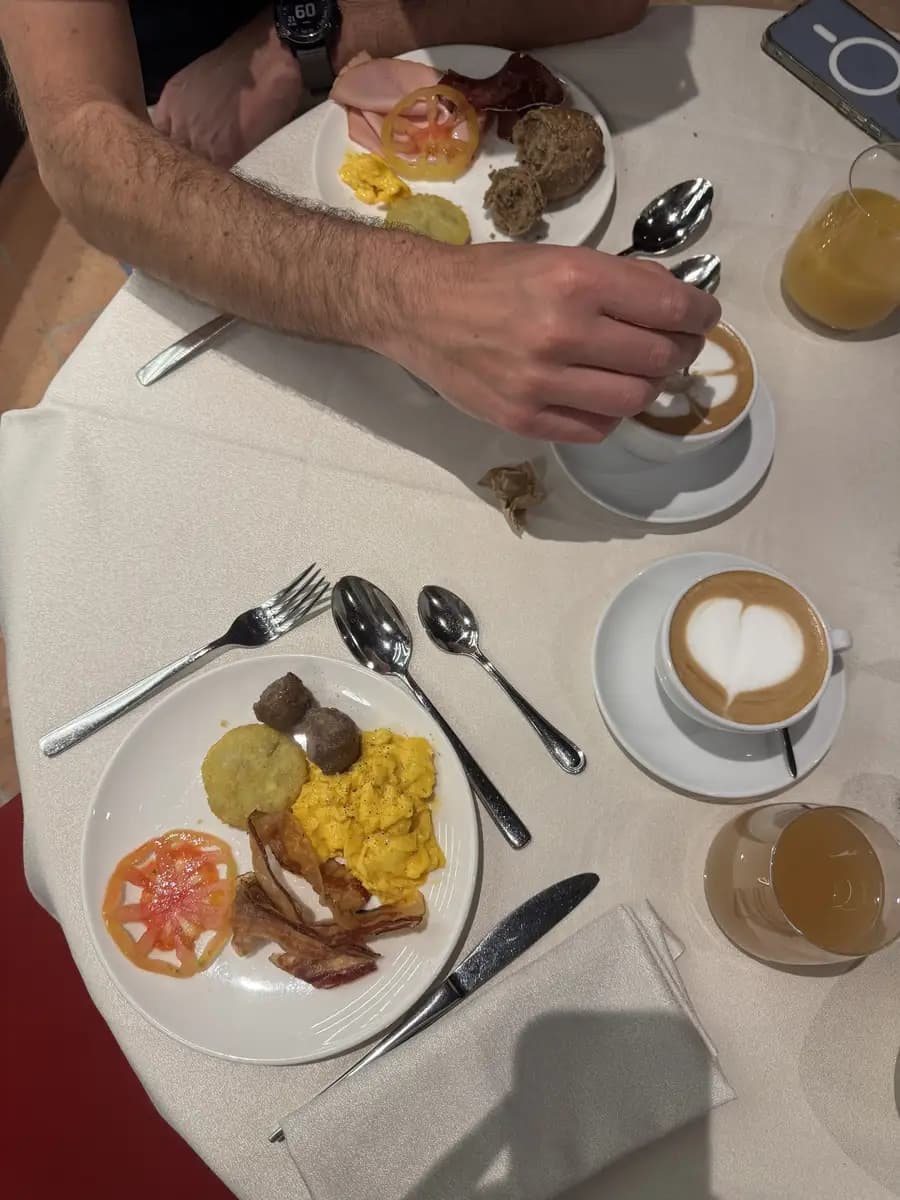 picture of breakfast capaccino, scrambled eggs, tomatoes, sausages, bacon and apple juice