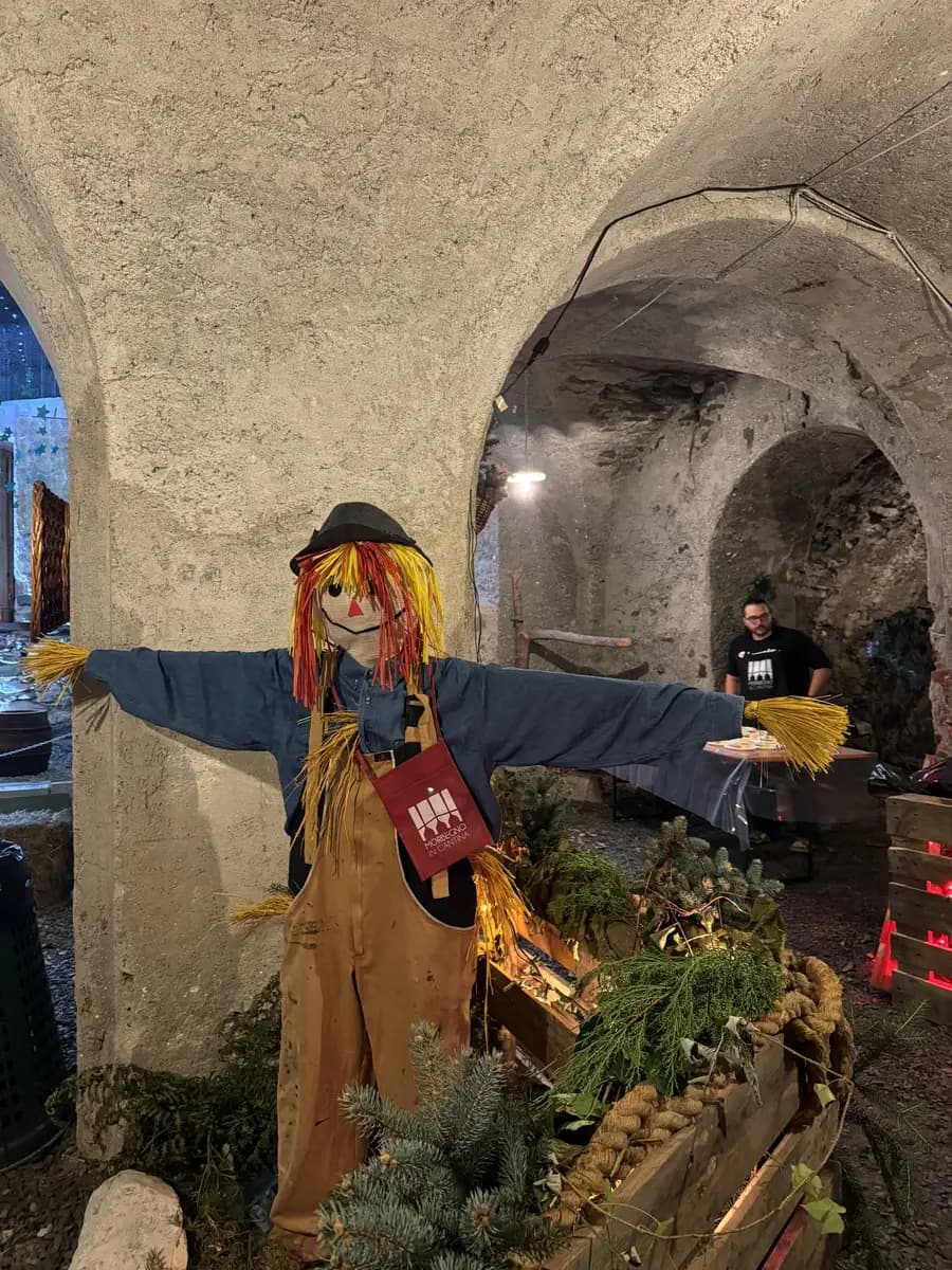 a scarecrow with a wine glass around his neck inside the wine cellar in morbegno