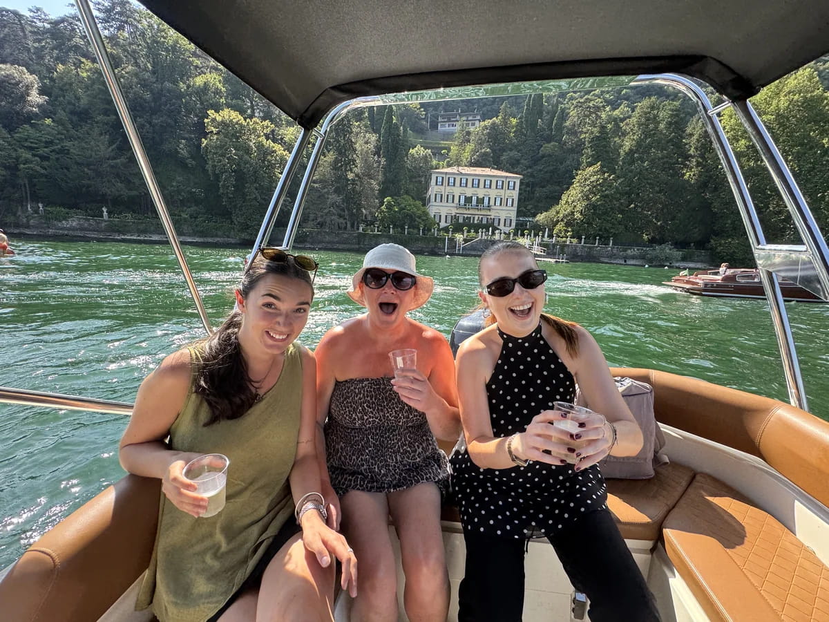 three women on a boat in lake como in front of the villa Versace with a glass of prosecco on a boat tour